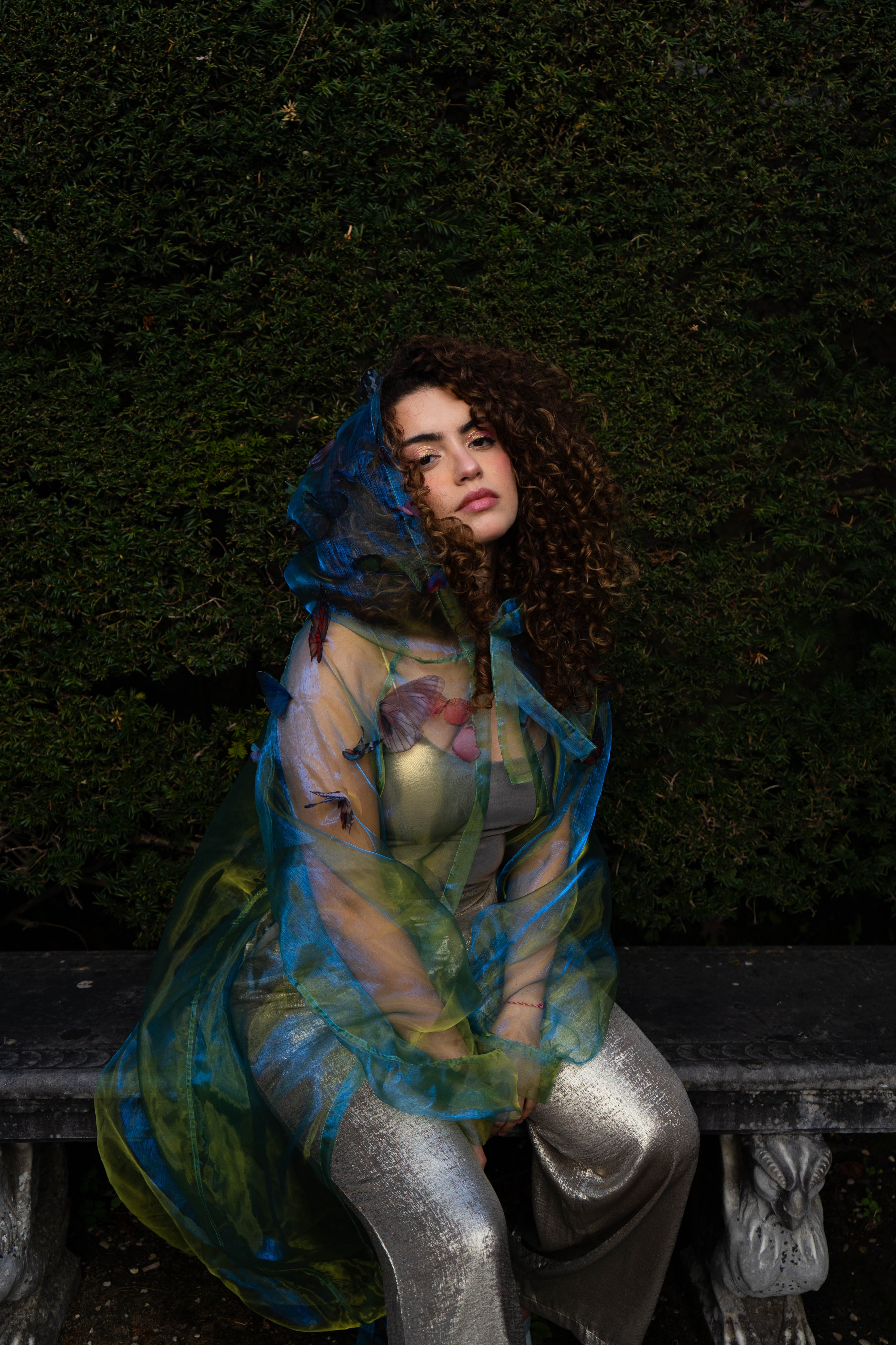 LA CAPE ÉTHÉRÉE — VERT BOREAL

Silhouette vaporeuse &amp; éclats magnétiques.

Voile iridescent de haute légèreté captant la lumière pour un effet holographique aux reflets vert d'eau et dorés.

Papillons découpés et cousus main individuellement, créant un relief organique et poétique sur l'ensemble de la pièce.

Chaque modèle est une pièce unique : le positionnement des papillons étant réalisé à la main, chaque cape possède sa propre constellation de motifs.
