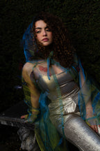 LA CAPE ÉTHÉRÉE — VERT BOREAL

Silhouette vaporeuse &amp; éclats magnétiques.

Voile iridescent de haute légèreté captant la lumière pour un effet holographique aux reflets vert d'eau et dorés.

Papillons découpés et cousus main individuellement, créant un relief organique et poétique sur l'ensemble de la pièce.

Chaque modèle est une pièce unique : le positionnement des papillons étant réalisé à la main, chaque cape possède sa propre constellation de motifs.
