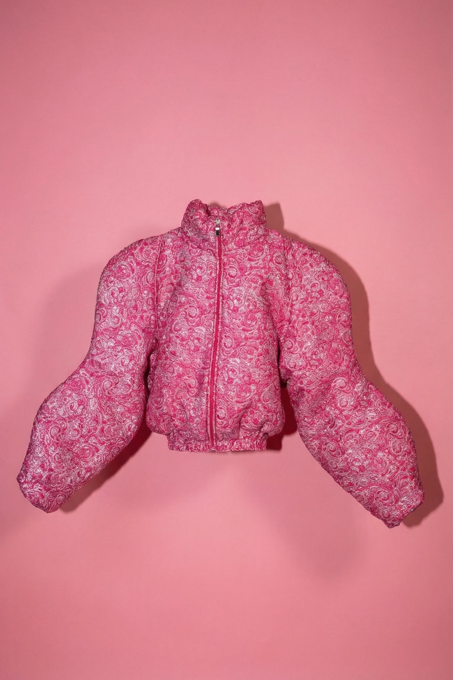 Doudoune rose texturée à effet serti argenté. Manches butterfly structurées. Rembourrage THERMO 180. Doublure satinée grise. Fermeture zippée, poches latérales. Edition limitée à 3 exemplaires